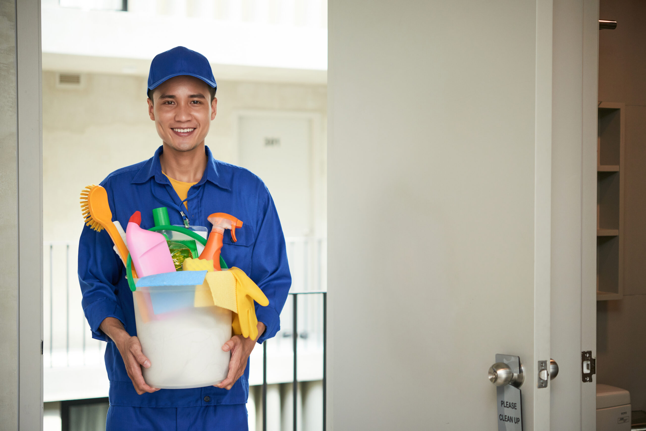 cheerful asian male janitor walking into hotel room carrying supplies bucket scaled