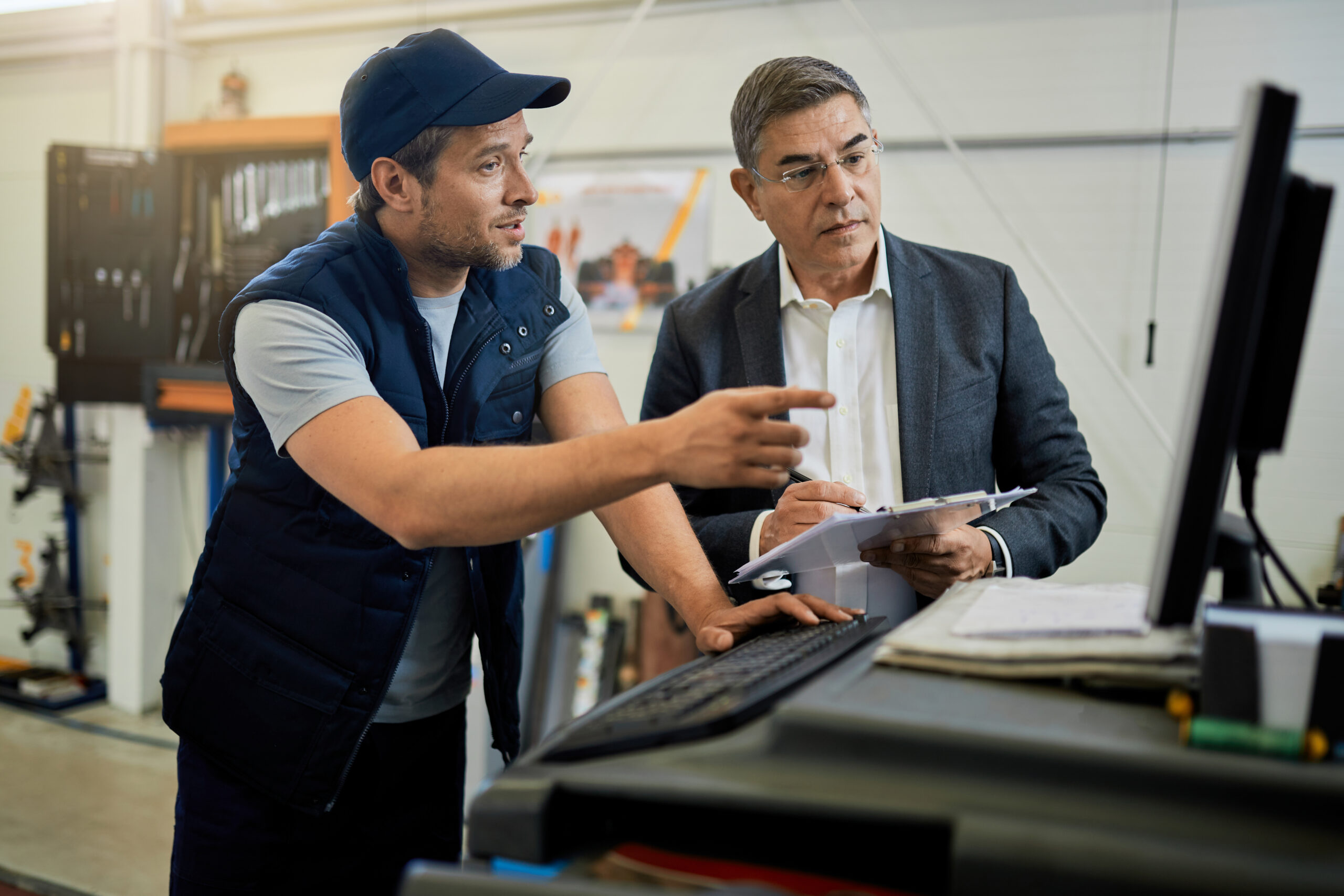 mid adult manager car mechanic talking while using computer auto repair shop scaled